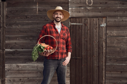 Farmer holding basket of organic vegetables by wooden shed outdoors