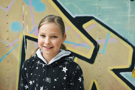 Smiling child in casual hoodie by graffiti wall in Berlin summer