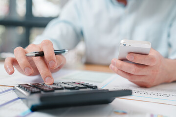 Close-up of a businessman calculating finances using a calculator and smartphone at the office. Concept of accounting, budgeting, finance, and business analysis.