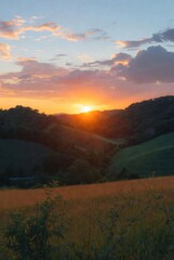 Spectacular golden sunset over lush green rolling hills and valleys. Beautiful evening landscape with a bright sun setting behind the horizon under a soft cloudy sky.