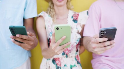 Group of unrecognizable diverse friends standing together against a yellow wall, each busy using their own mobile phone for social media - Powered by Adobe