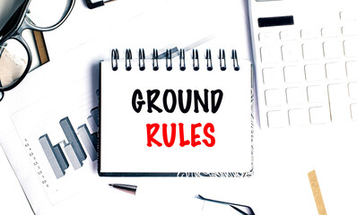 Notebook with text ground rules on office desk with documents, glasses, pen, and keyboard,
