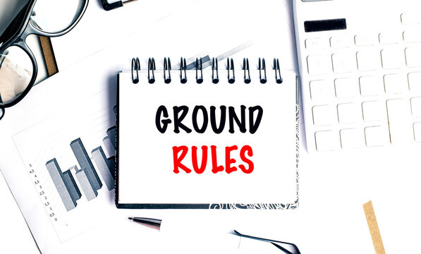 Notebook with text ground rules on office desk with documents, glasses, pen, and keyboard,