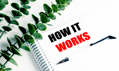 Notebook with text how it works on white desk with green leaves and pen, symbolizing explanation, process
