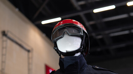 Mannequin with red helmet closeup showing polished visor and protective uniform on industrial exhibition stage with moody lighting, reflective surfaces, gear details and realistic turnout