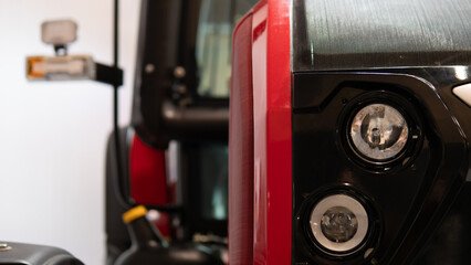 closeup red scooter headlight and dashboard showing polished chrome and glossy paint, indoor showroom or garage setting, mirror and control panel visible, compact electric vehicle prepped