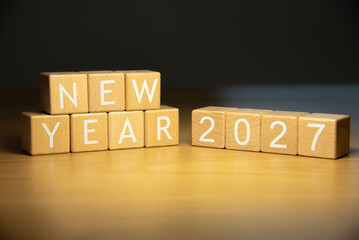 Wooden cube blocks HNY 2027 with Christmas tree defocused background. Texts and numbers on wooden blocks with copy space. 2026 happy new year idea concept.