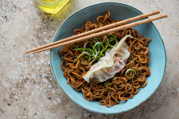 Ramen served with steamed dumpling in a turquoise bowl, horizontal shot on a beige granite background, top view