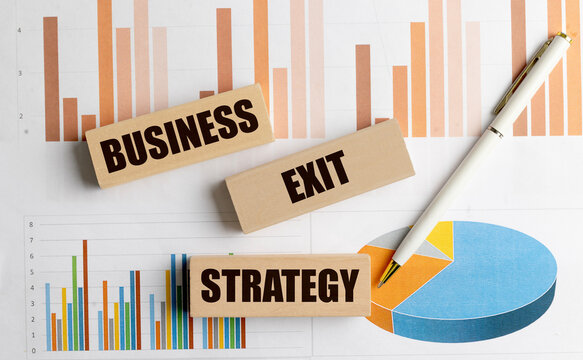 Wooden blocks with text business exit strategy on financial charts with white pen symbolizing planning and company transition