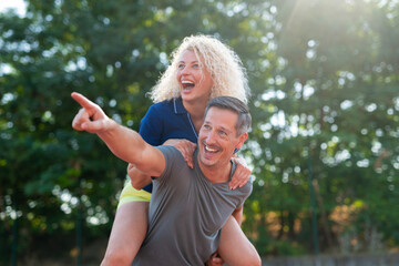Happy couple enjoying piggyback ride outdoors pointing