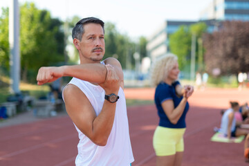 Man and woman stretching arms on a running track