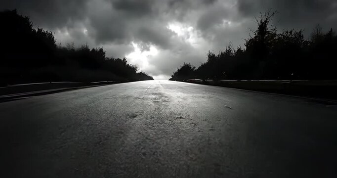 A low-angle shot of a zebra crossing on a wet road under a dramatic, cloudy sky in monochrome.