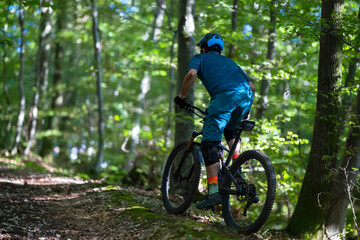 Fototapeta premium Cyclist riding an electric mountain bike through a lush forest trail on a sunny day