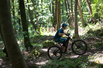 Person rides an electric mountain bike through a sunlit forest trail wearing a helmet
