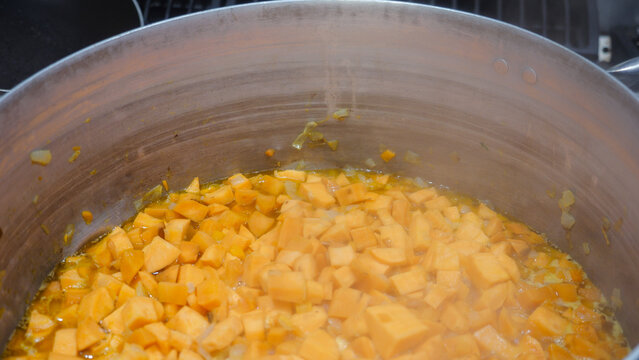 Sweet potato cubes are simmering in a large aluminum pot on a commercial gas stove, creating a flavorful broth for traditional African dishes in a professional kitchen setting