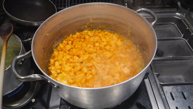 Sweet potato cubes are simmering in a large aluminum pot on a commercial gas stove, creating a flavorful broth for traditional African dishes in a professional kitchen setting
