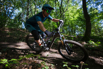 Mountain biker on an electric mountain bike rides through a forest trail in sunlit foliage
