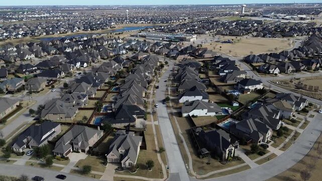 Curving residential streets in Prosper, Texas form cohesive layout of single-family homes with varied rooflines, backyard pools, central playground. Commercial buildings, water tower at horizon