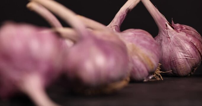 ripe purple garlic is scattered on a black table in the kitchen, garlic spices are on a slate board in the kitchen over cooking