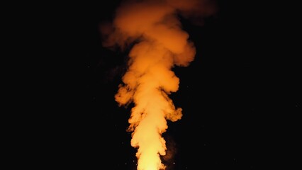Smoke rises from a volcanic eruption at night near a lava flow creating an orange glow in the sky