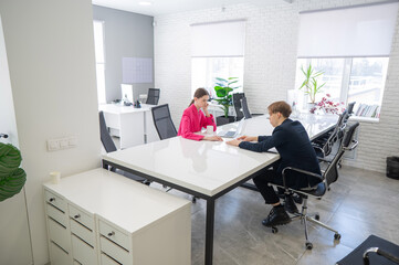 Man and woman talking while sitting at desk in office. 