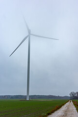 Fototapeta premium A wind turbine on a cloudy autumn day. Low-hanging clouds partially cover the rotor blades.