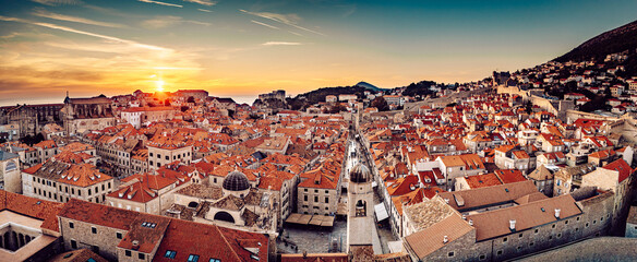 Aerial view of terracotta rooftops cascading toward the sea, embraced by ancient stone walls under a vibrant sunset sky, Dubrovnik, Dubrovnik-Neretva County, Croatia.