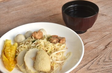 dry boiled Chinese yellow egg noodles dory fish and fishball with bean sprout topping crispy dumpling on plate and soup in cup