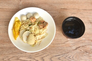 dry boiled Chinese yellow egg noodles dory fish and fishball with bean sprout topping crispy dumpling on plate and soup in cup
