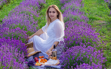 Woman with a glass of wine having a picnic in a lavender field at sunset