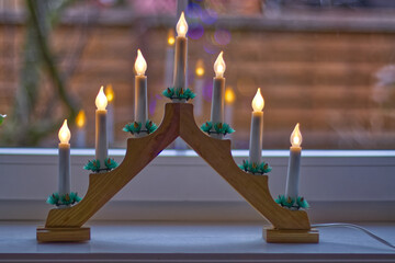 An electric Christmas candlestick standing on a windowsill inside a room.