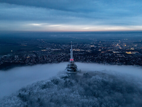 Aerial view of the iconic Zobor transmitter piercing through a sea of fog, casting a glow over the city, Nitra, Nitra Region, Slovakia.