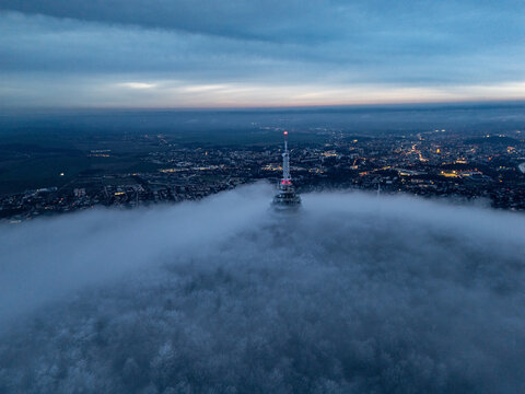 Aerial view of the towering Zobor transmitter piercing through a sea of ethereal fog beneath a somber twilight sky, Nitra, Nitra Region, Slovakia.
