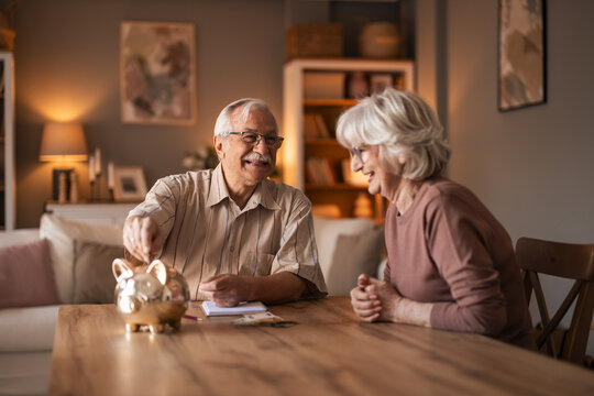 Warm Home Moment: Elderly Couple Smiles At Table With Piggy Bank And Papers - Powered by Adobe