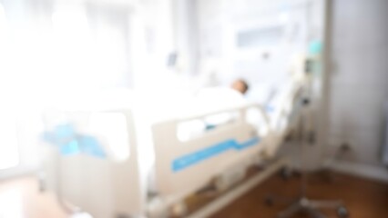 Blurry hospital ward scene with patient in bed and IV pole