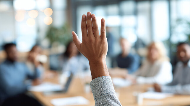 Close up of a person raising their hand in a meeting, asking a question, volunteering or suggesting an idea in business setting with other people.