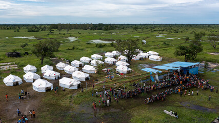 Aerial view of a large group of people lining up near a tent city amidst a landscape of green and brown, Dondo, Sofala Province, Mozambique.