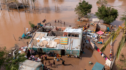 Aerial view of murky floodwaters engulfing homes, with only rooftops visible amid scattered debris and displaced people seeking refuge, Sofala Province, Mozambique.