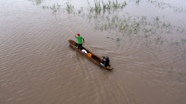 Aerial view of two figures navigating the murky waters in a slender canoe, a scene of quiet determination against the backdrop of Sofala Province, Mozambique.