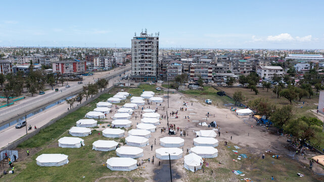 Aerial view of a tent city sprawling beneath the city's skyline, a stark contrast of temporary shelters against the backdrop of permanent buildings, Beira, Sofala Province, Mozambique.