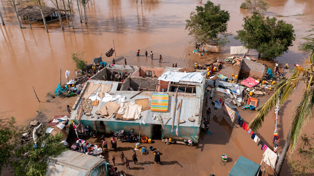 Aerial view of murky floodwaters engulfing homes, with only rooftops visible amid scattered debris and displaced people seeking refuge, Sofala Province, Mozambique.