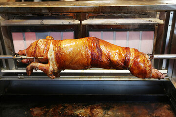Grilled suckling piglet in spit roast. Traditional whole pig roasted on barbecue spit. Popular delicious and crispy roasted piggy on christmas fair