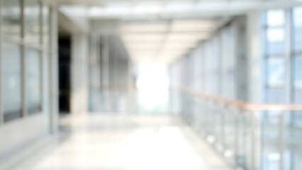 Blurry modern office hallway with glass walls and bright light at end