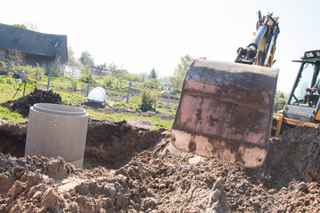 Tractor at the construction site lowers the second concrete ring for the well into a dug trench, drinking water well