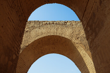 Fototapeta premium Low-angle, symmetrical view of the Bahram Fire Temple in Shahr-e Ray, highlighting its layered historical architecture against a clear blue sky.
