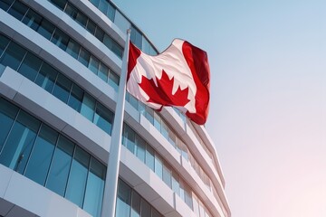 A glass building stands tall under clear skies with the flag of Canada waving above. The flag is brightly colored and visible from a distance in the city