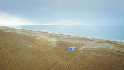 Aerial view of a lone blue structure stands out against the vast expanse of sandy beach meeting the tranquil sea, Narbonne plage, France.
