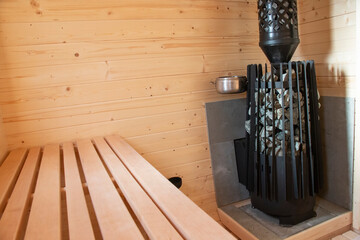 Light, spacious sauna made of natural wood with a stove. Modern boiler filled with sauna rooms