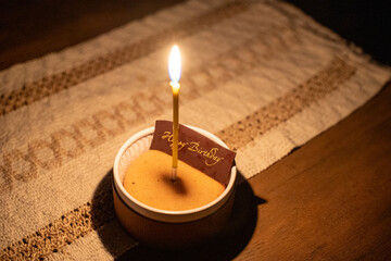 Single candle on birthday cake in dim lighting