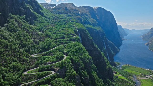 Aerial view of Trollstigen road above Geirangerfjord in Norway. Drone footage shows dramatic mountain curves, steep cliffs and deep blue fjord on a clear summer day.